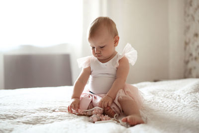 Toddler baby in a dress with beads playing on a bed in a real interior