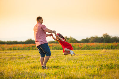 Father playing with daughter on field against sky