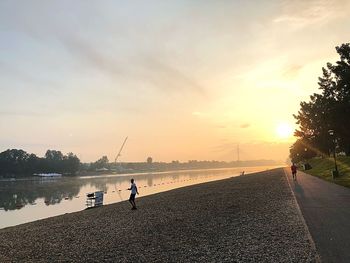 People on shore against sky during sunset