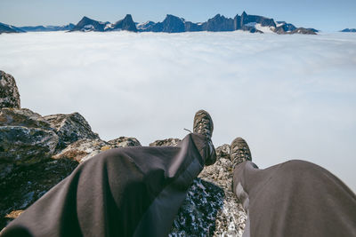 Low section of man sitting on mountain with clouds in background