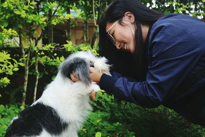 Side view of young woman holding dog against plants