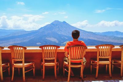 Rear view of man sitting on chair against mountains