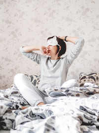 Young woman in grey pajama and sleeping mask in shape of cute sleeping cat face. she is just woke up