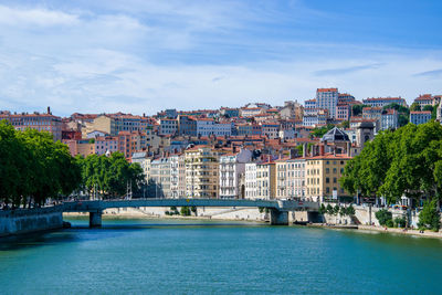 Buildings by river against sky in city