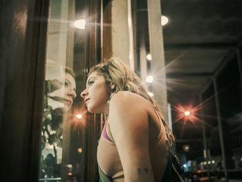 Side view of young woman looking through window