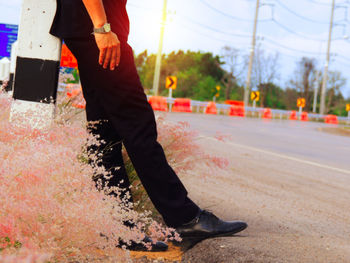 Low section of man standing by flowers at roadside