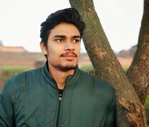 Portrait of young man standing against tree trunk