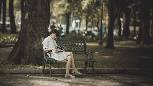 Woman reading book while sitting on bench at park