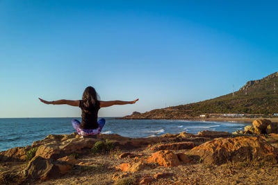 Full length of person on rock at beach against clear blue sky