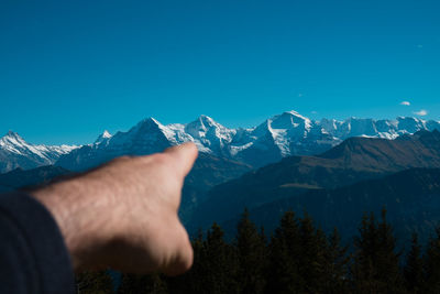 Midsection of person on snowcapped mountain against blue sky