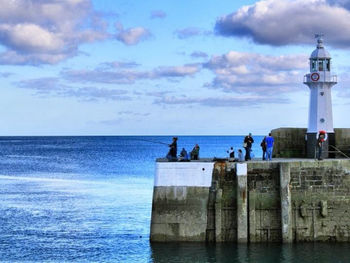 Lighthouse in sea against cloudy sky