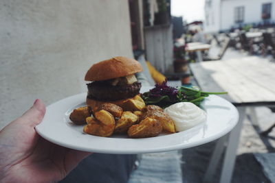 Cropped image of hand holding hamburger in plate