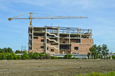 Low angle view of crane by building against sky