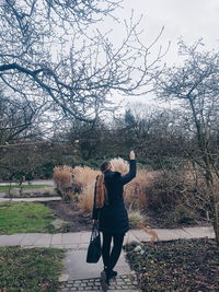 Rear view of woman standing by bare tree against sky