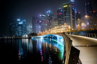 Illuminated footbridge over river against skyscrapers