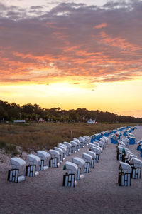 Chairs on beach against sky during sunset