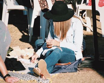 Woman with drink sitting on field during sunny day