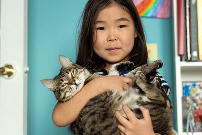 Child portrait with domestic pet, cute asian girl holding tabby cat