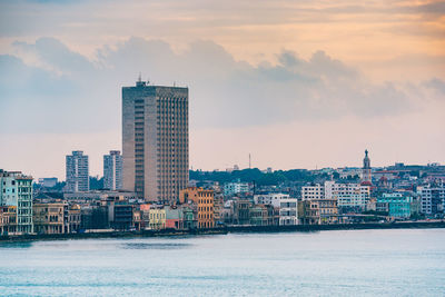 City by river against cloudy sky during sunset