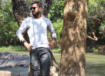 Young man standing by tree trunk in forest