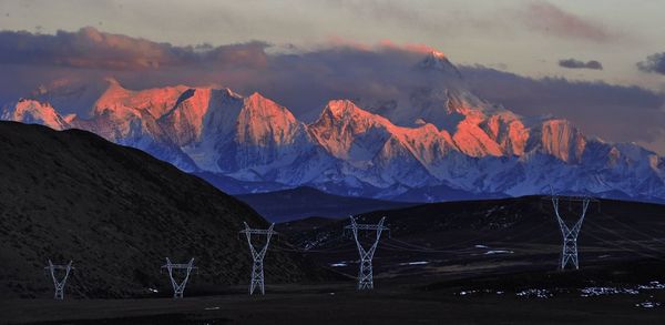 Electricity pylons on field against mountains during sunrise