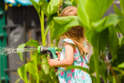 2-3 year old girl with garden hose water the plants plants. activity for chirldren at summer 
