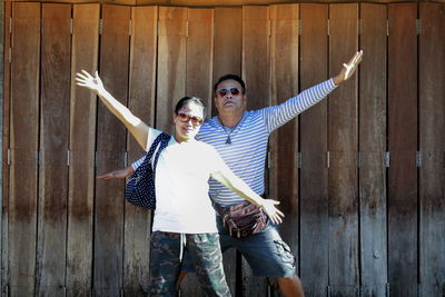 Couple with arms outstretched standing against wooden fence