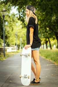 Side view of woman with skateboard standing at park 