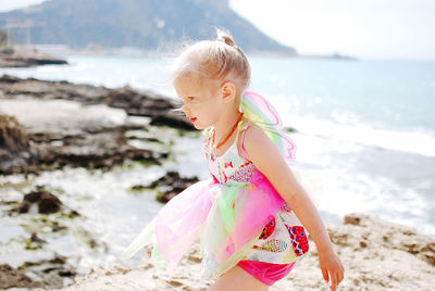 Portrait of little blondie girl in butterfly costume standing at beach