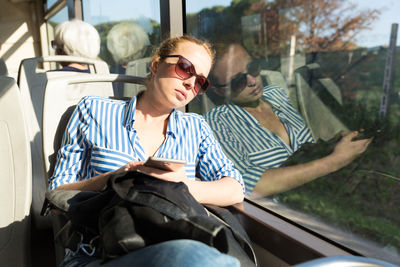 Mid adult woman wearing sunglasses sleeping at bus