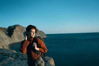 Young woman standing by sea against sky