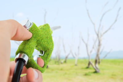 Cropped hand of person holding fuel pump against sky