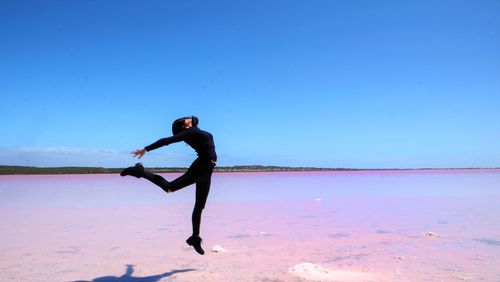 Side view of woman jumping over pink lake against blue sky