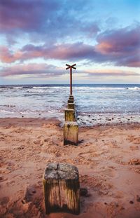 Wooden posts on beach against sky during sunset