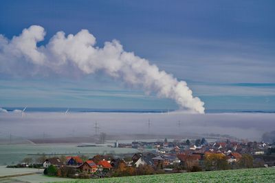 Smoke emitting from chimney on landscape against sky