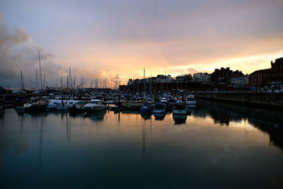 Boats moored at harbor against cloudy sky during sunset