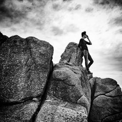 Low angle view of teenage boy standing on cliff against cloudy sky