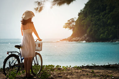 Rear view of woman with bicycle standing by sea