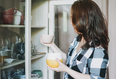 Side view of mature woman arranging bowls on shelf at home