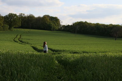 Side view of young woman standing amidst green crop on field