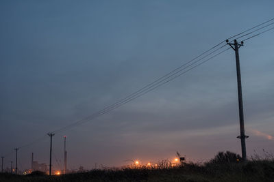 Low angle view of electricity pylons on field against sky during sunset