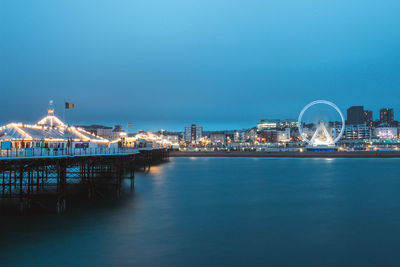 Illuminated city by sea against clear sky at night