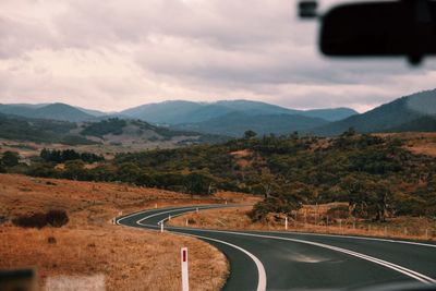 Empty road leading towards mountains seen through car windshield