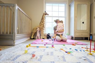 Young mother and daughter hug in nursery with toys and crib