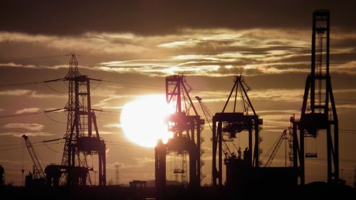 Silhouette cranes and electricity pylons against sky during sunrise