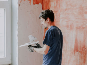 A caucasian guy puts putty on a spatula against the background of prepared walls with a red mortar