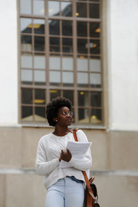 Young woman looking away while standing against wall