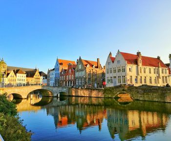 Bridge over river by buildings against blue sky