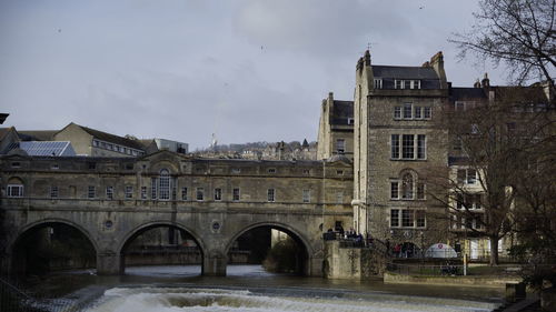 Arch bridge over river by buildings against sky in city