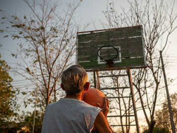 Rear view of man with basketball hoop against trees